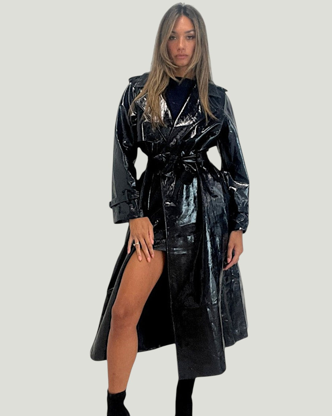 Model draagt een glanzende zwarte Mademoiselle Ambitious Basile jas met ceintuur en normale pasvorm.