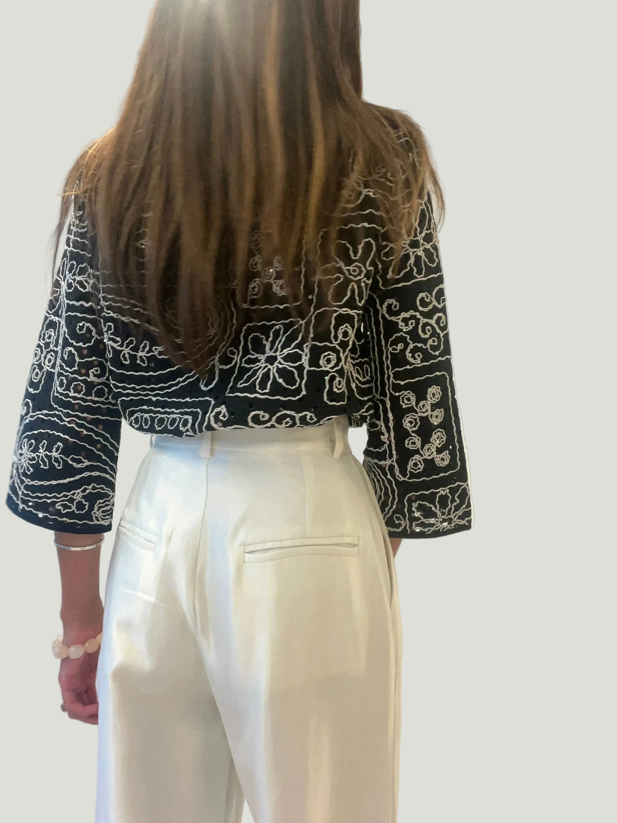 Mademoiselle Ambitious Hanna blouse in zwart met wit borduurwerk, gedragen met een witte broek, rugaanzicht.