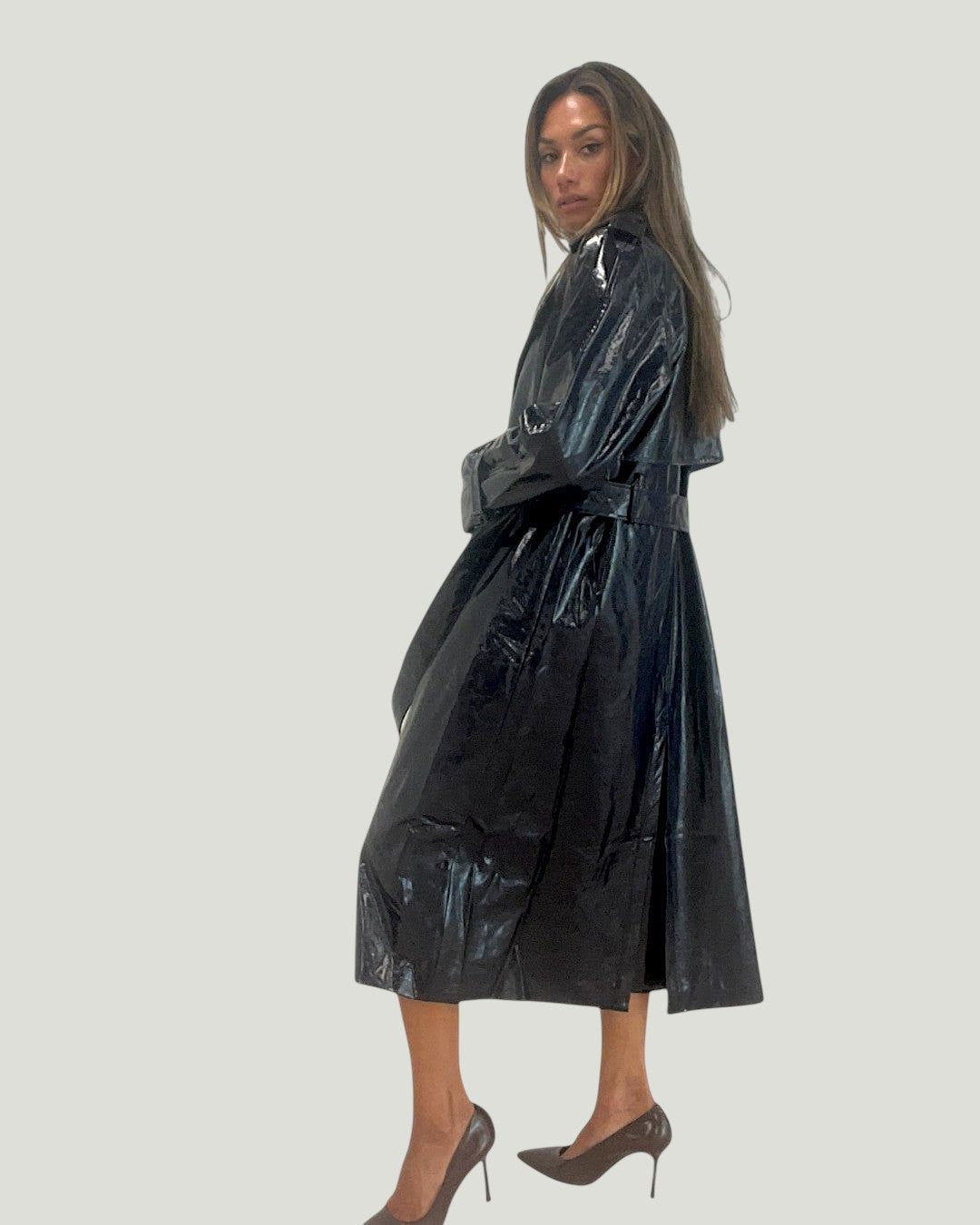 Model draagt een glanzende zwarte Mademoiselle Ambitious Basile jas van PU en rayon met een ceintuur