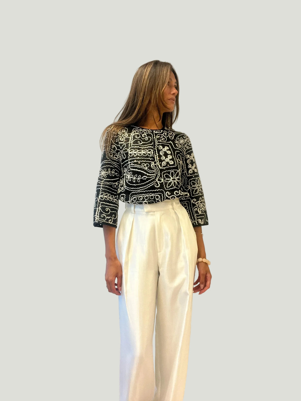Mademoiselle Ambitious Hanna blouse in zwart met wit borduurwerk, gedragen met een witte pantalon door een model.